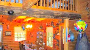 A rustic cabin interior with a dining area, wooden walls, and a staircase.