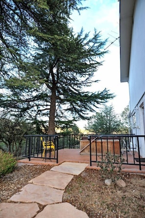 A stone pathway leading to a wooden deck with a yellow chair, surrounded by trees and a white building.