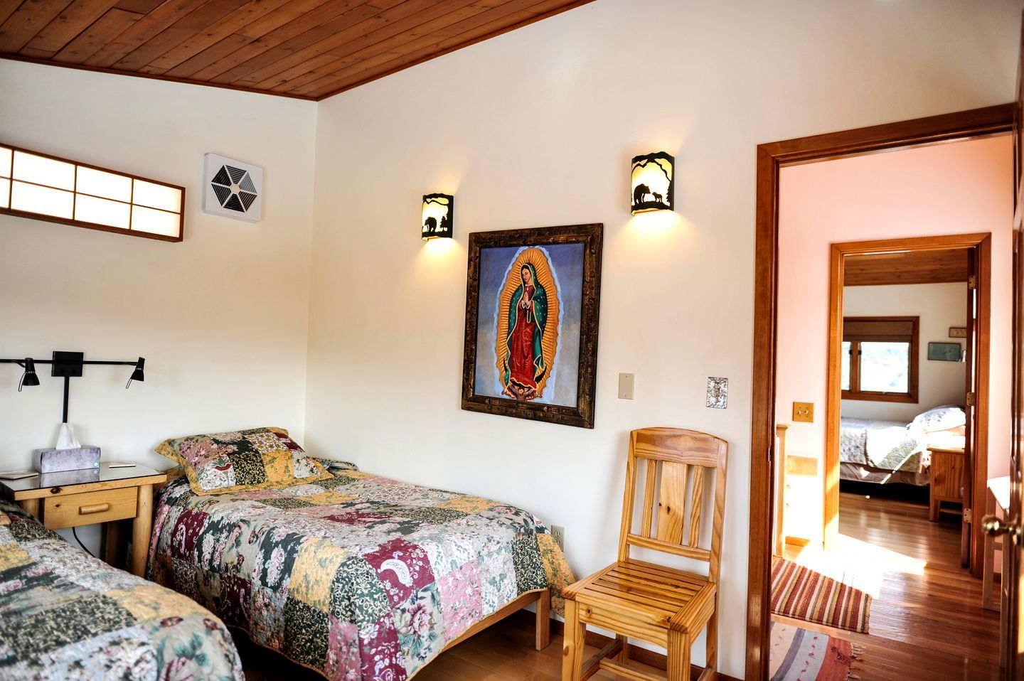 A bedroom with two beds, a wooden chair, a wall-mounted picture, and a door leading to another room.