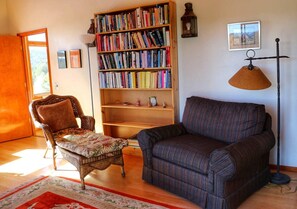 A cozy living room with a bookshelf, a patterned armchair, a sofa, a floor lamp, and a rug. - Peaceful Luxury Vacation Rental near Gila National Forest in Silver City, New Mexico (Silver City)