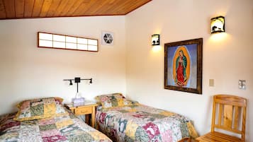 Una habitación con dos camas, una silla de madera, una mesita de noche, un respiradero en la pared y un cuadro enmarcado.