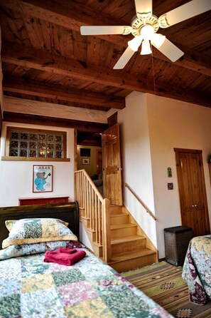 A bedroom with a wooden ceiling, a bed with a floral quilt, a wooden staircase, and a ceiling fan. - Upscale Family-Friendly Vacation Rental with Spectacular Desert Views in New Mexico (Silver City)