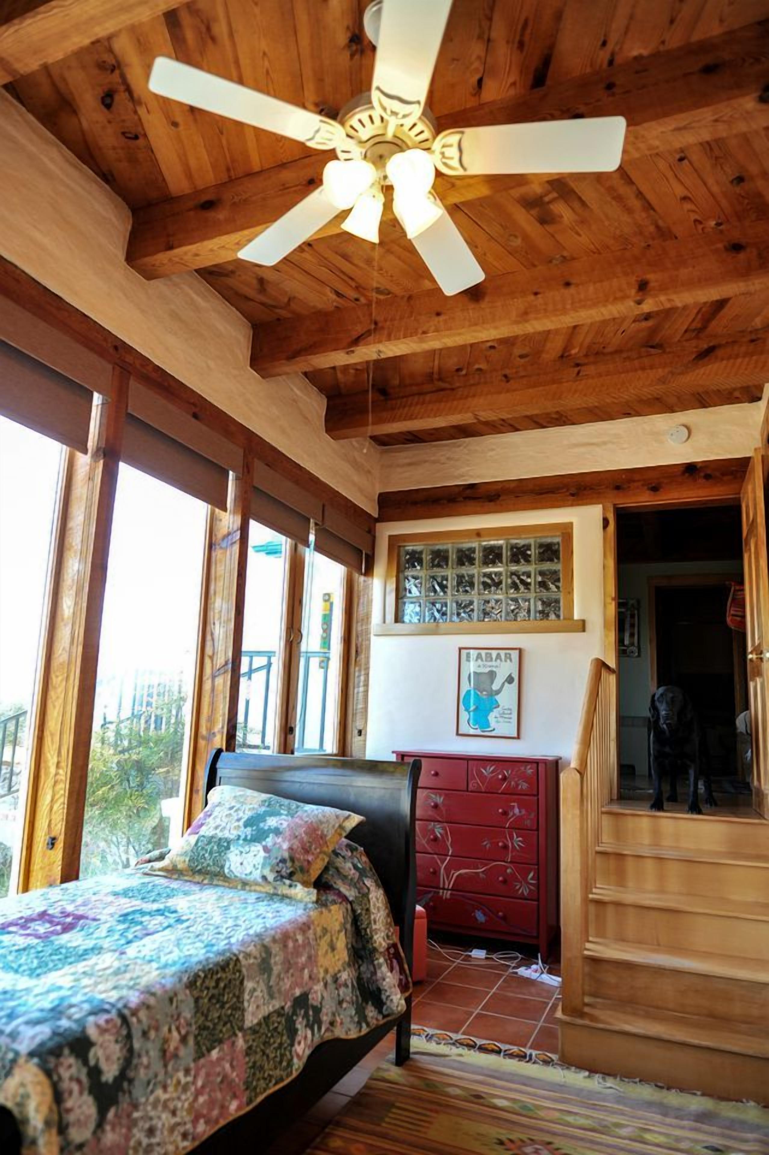 A bedroom with a bed, a ceiling fan, a dresser, and a window with a view.