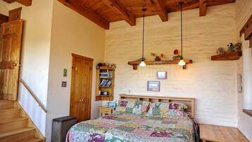 A bedroom with a wooden staircase, a bed with a floral quilt, a bookshelf, and a wooden ceiling.