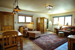 A spacious living room with a large window, a wooden dining table, a sofa, and a rug.
