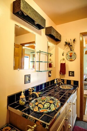 A bathroom with a black tiled sink, a mirror, and a decorative plate.