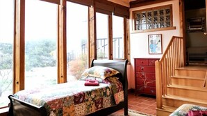 Ein Schlafzimmer in einer Holzhütte mit einem Bett, einer Bank, einer Treppe und Blick durch große Fenster.