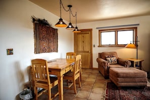 Un coin repas avec une table et des chaises en bois, un tapis à motifs, un canapé et une fenêtre donnant sur un paysage agréable.