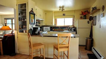 A kitchen with a central island, two bar stools, a stove, microwave, and various kitchen items.