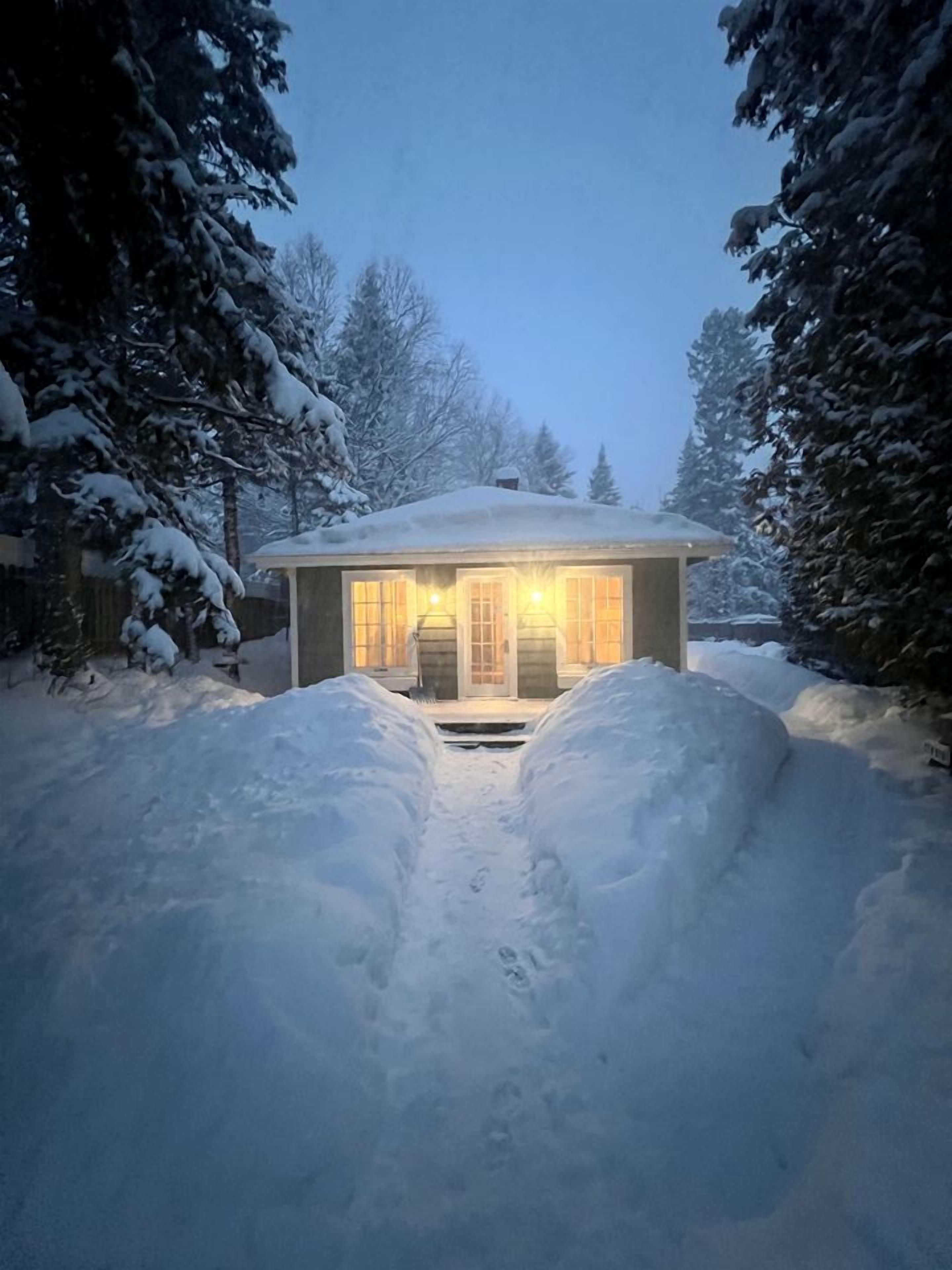 Un camí cobert de neu que condueix a una casa amb l'entrada il·luminada.