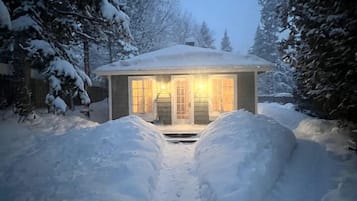 Un sentier enneigé menant à une maison dont l’entrée est illuminée.