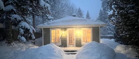 Un sendero cubierto de nieve que lleva a una casa con la entrada iluminada.