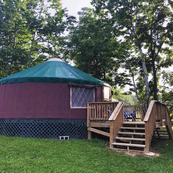 A yurt with a green roof, a small window, and a wooden deck with stairs leading up to it.