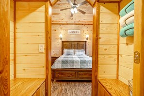 A wooden cabin room with a bed, a ceiling fan, and a wall-mounted towel rack.