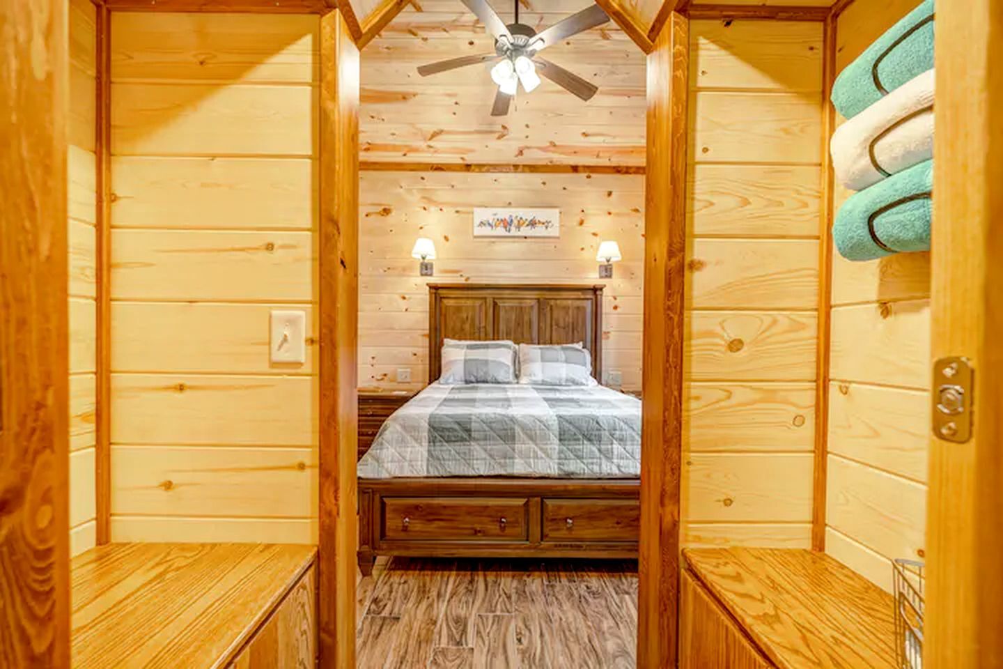 A wooden cabin room with a bed, a ceiling fan, and a wall-mounted towel rack.