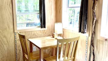 Un interior de madera con una mesa y sillas, dos ventanas con cortinas y un cuadro en la pared.