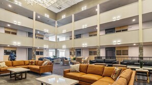 Een ruime lobby met meerdere zithoeken, een hoog plafond met verlichting, en een modern architectonisch ontwerp.