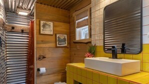 Un baño pequeño con techo de madera, inodoro blanco, lavabo con azulejos amarillos y un espejo.