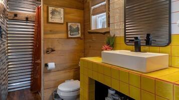 A compact bathroom with a wooden ceiling, a white toilet, a yellow tiled sink, and a mirror.