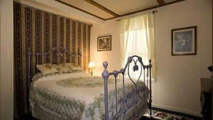 Une chambre à coucher avec un lit, des rideaux, une lampe et un tableau au mur.