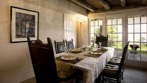Une salle à manger avec une longue table dressée pour six personnes, des chaises en bois, un tableau encadré au mur et une vue dégagée grâce à de grandes fenêtres.