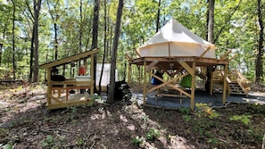 Un terrain de camping situé dans une forêt, avec une tente et une structure en bois, qui pourrait être un abri de rangement, ainsi qu'une table et des chaises.
