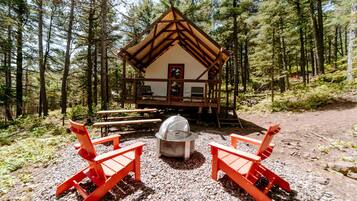 A cabin with a wooden deck, two red chairs, a picnic table, and a grill.
