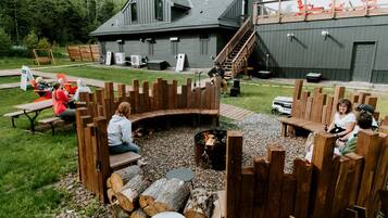 A rustic outdoor seating area with wooden benches and a fire pit, surrounded by a wooden fence.