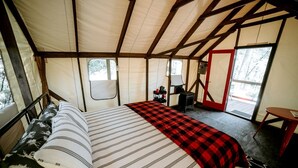 A tent with a bed, a table, and a stove. - Glamping Safari Tent for Romantic Escapes to the Minnesota Forest (Beaver Bay)