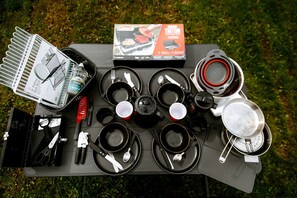 Equipo de campamento que incluye un hornillo portátil, utensilios de cocina y un escurreplatos plegable.