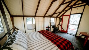 A tent with a bed, a table, and a stove. - Glamping Safari Tent for Romantic Escapes to the Minnesota Forest (Beaver Bay)