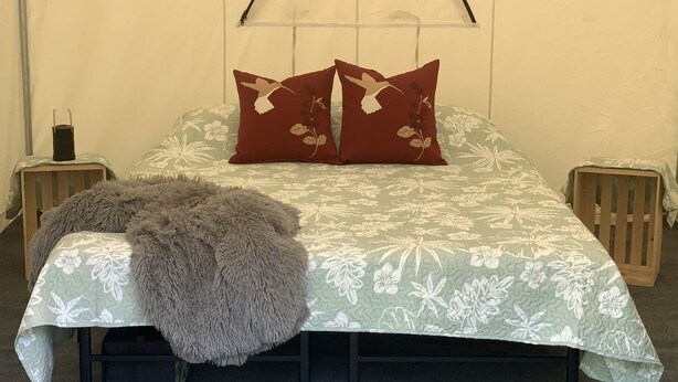 A bed with a floral bedspread, two pillows with a bird design, a fluffy throw, and two nightstands with candles.
