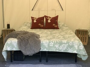 A bed with a floral bedspread, two pillows with a bird design, a fluffy throw, and two nightstands with candles. - Cozy Secluded Safari Tent Immersed in Nature in Ravenna, Ohio (Ravenna)