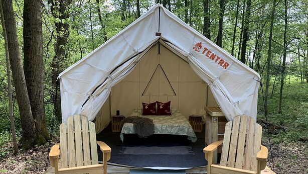 A tented accommodation with a bed, two chairs, and a small table.
