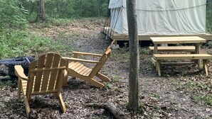 A tent, a wooden chair, and a picnic table in a forest.