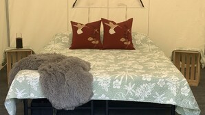 A bed with a floral bedspread, two pillows with a bird design, a fluffy throw, and two nightstands with candles.