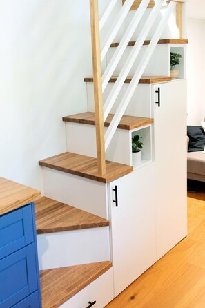 A staircase with wooden steps and white walls, leading to a room with a sofa and a plant.