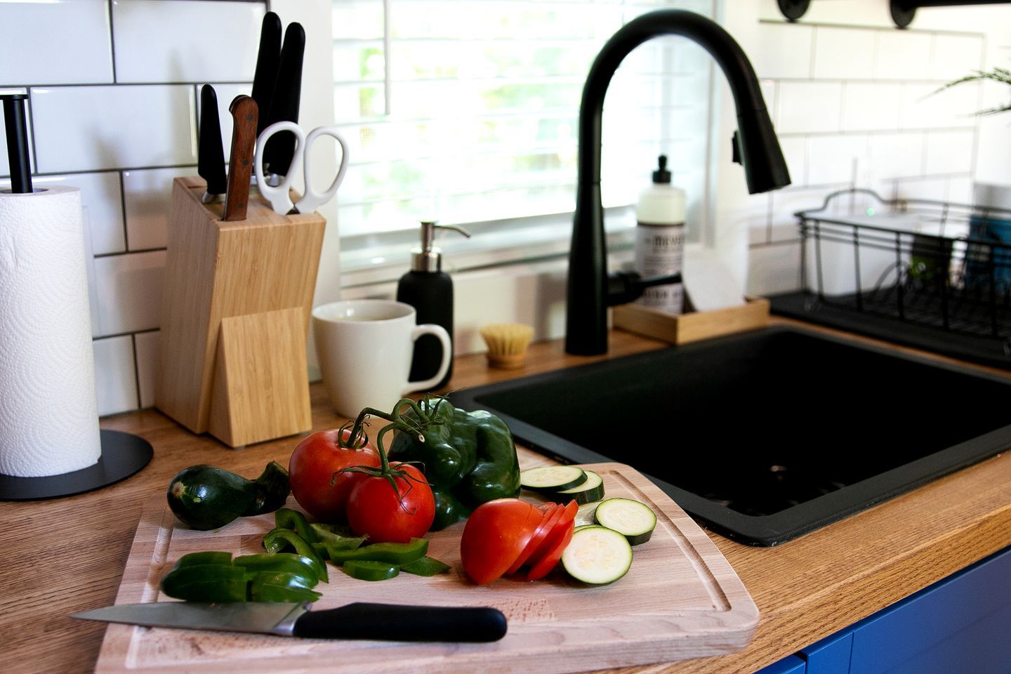 A kitchen counter with a cutting board, vegetables, and a knife.