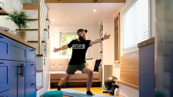 A person exercising on a mat in a room with a sofa, a plant, and exercise equipment.