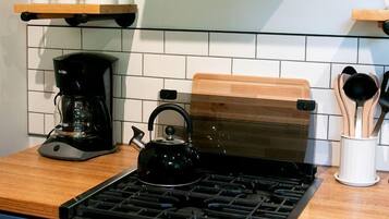 Una cocina con estufa a gas, cafetera y estantes de madera.