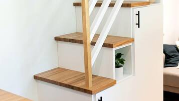 A staircase with wooden steps and white walls, leading to a room with a sofa and a plant.