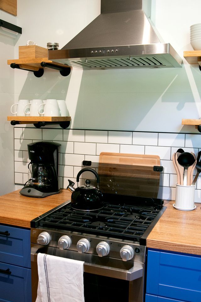 A kitchen with a gas stove, a coffee maker, and wooden shelves.