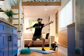 A person exercising on a mat in a room with a sofa, a plant, and exercise equipment.