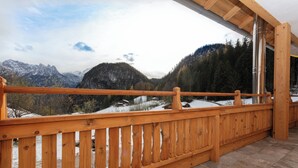 Un balcone in legno con vista su montagne innevate e una valle boscosa.