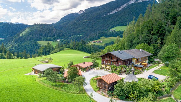 Un rifugio alpino con diversi edifici in legno, circondato da prati verdi e fitte foreste.