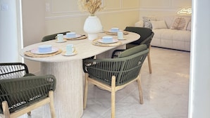 Een eethoek met een ronde tafel, stoelen en een vaas met gedroogde bloemen.