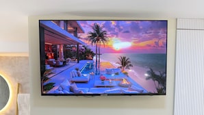 Een flatscreen televisie bevestigd aan een muur boven een open haard, met een beeldscherm dat een zonsondergang op het strand toont.