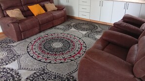 A living room with a brown leather sofa, patterned rug, and white cabinets. - Le Tai Village Homestay (Mweiga)