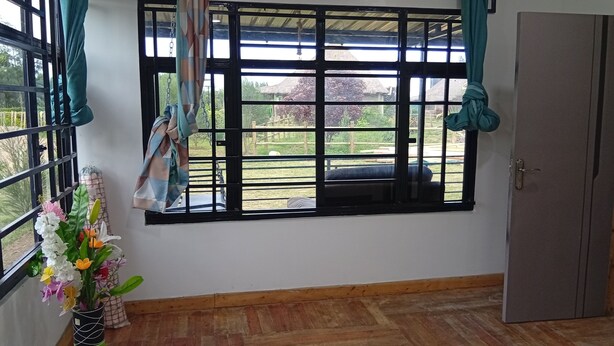 A room with a large window, a wooden floor, and a green vase with flowers. - Le Tai Village Homestay (Mweiga)