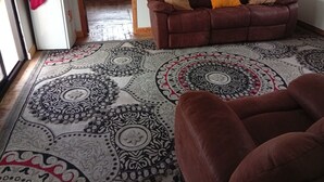 A living room with a patterned rug, a brown sofa with cushions, and a white cabinet. - Le Tai Village Homestay (Mweiga)